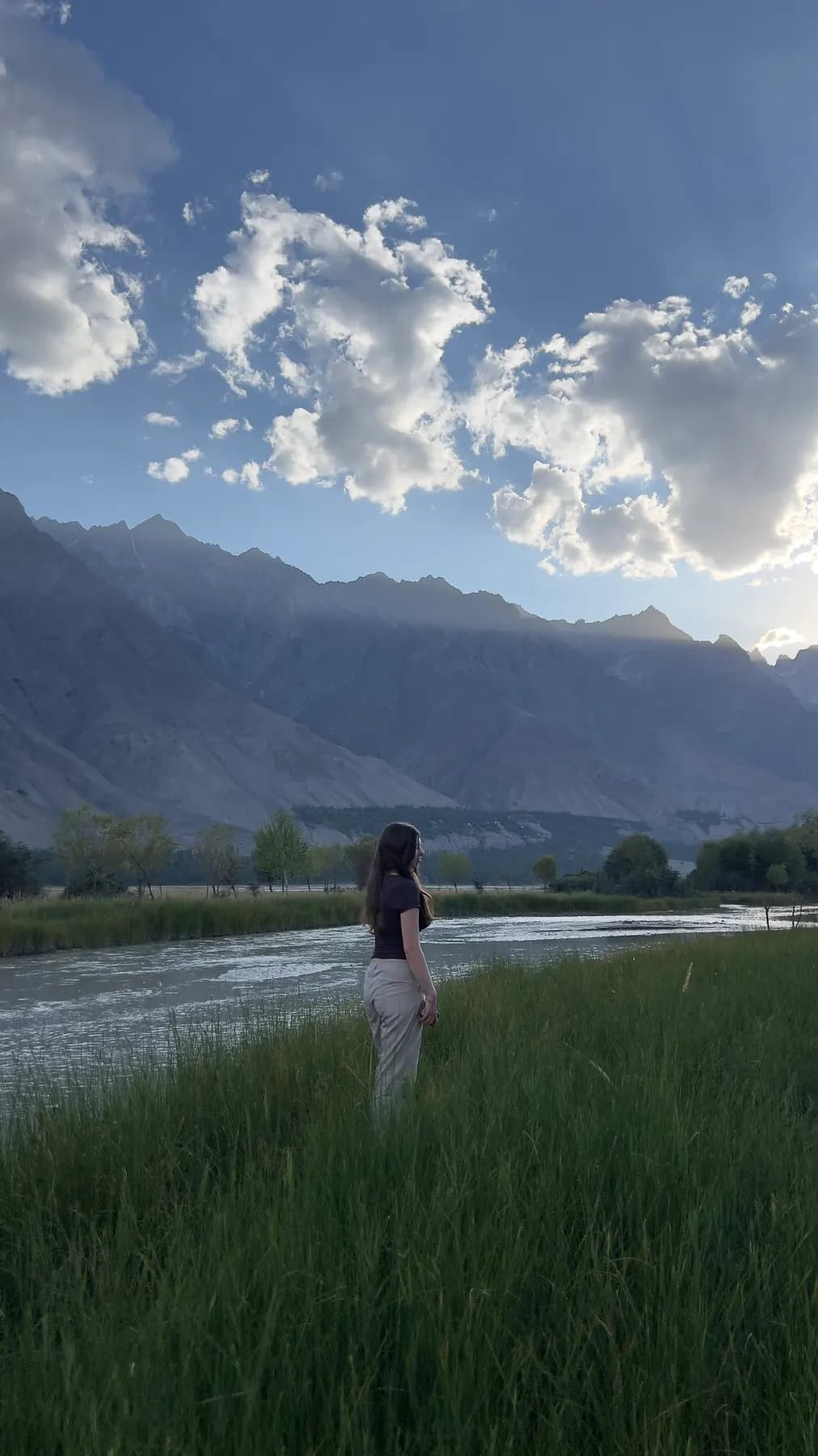 A guest in the riverside grass facing the mountains