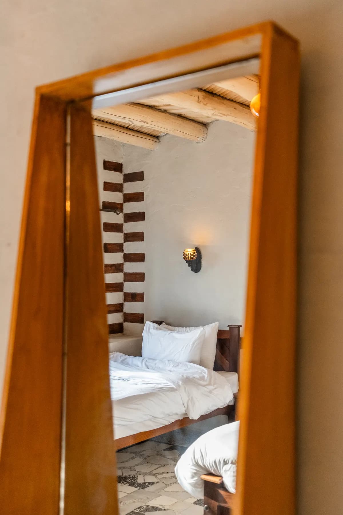 A bed reflected in a wooden standing mirror