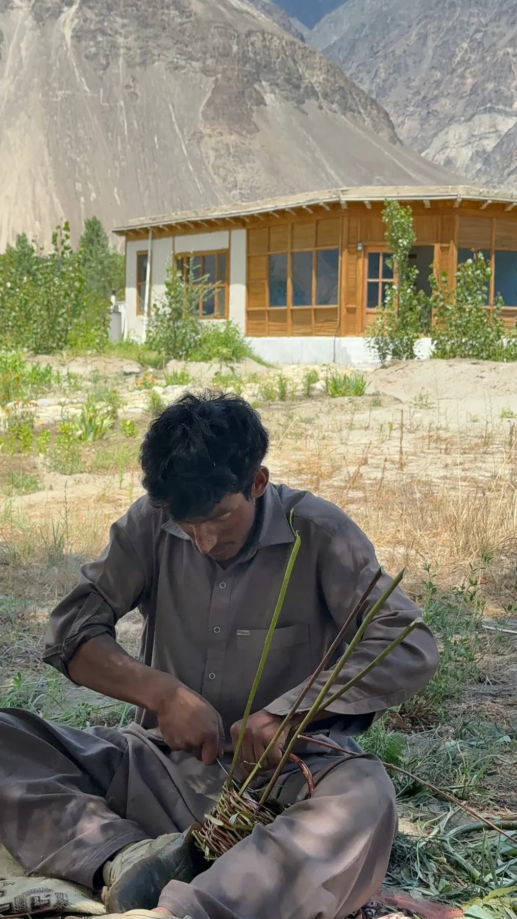A craftsman weaving a willow basket beside the lodge